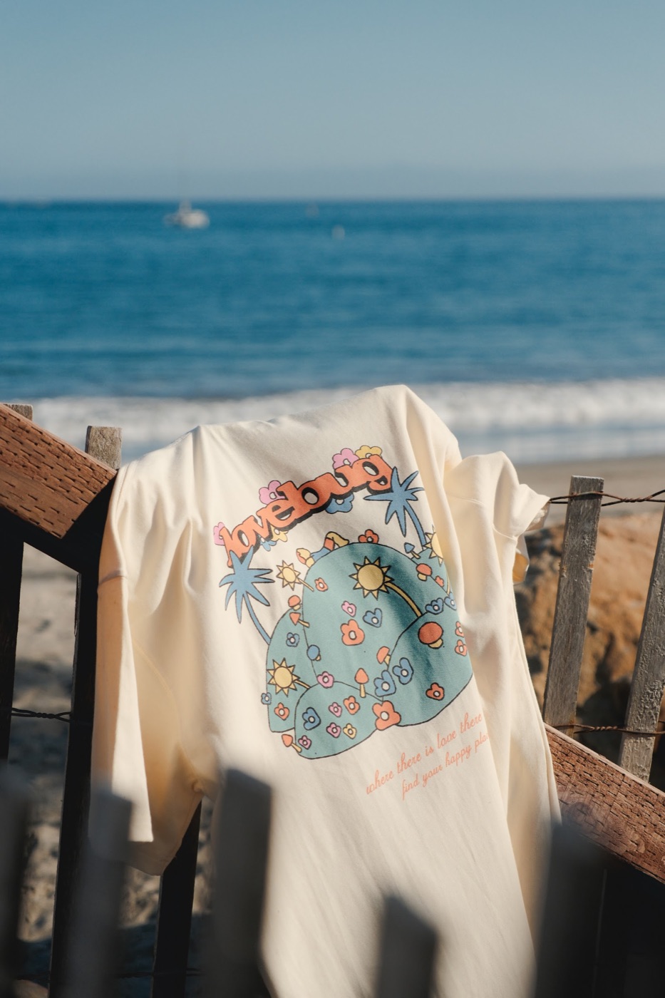 Lovebug Happy Place Tee on a beach fence in Santa Barbara